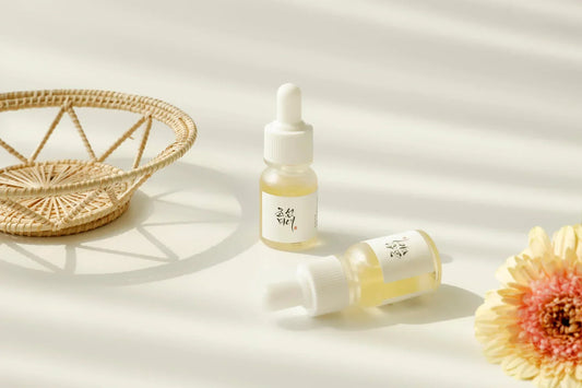Two small bottles of Beauty of Joseon Glow Serum Propolis + Niacinamide on a white table beside a rattan basket and a flower