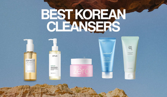 Title card reading Best Korean Cleansers with five cleansers lined up on a rock ledge against a blue sky: two cleansing oils, the Banila Co balm, the Medicube foam and the Beauty of Joseon gel